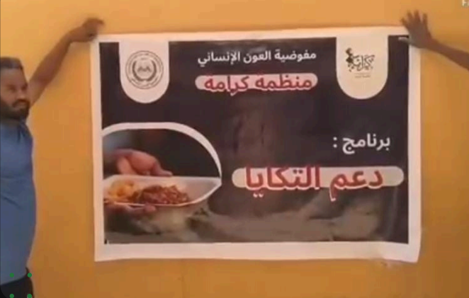 طاقم كرامة يُثبّت لافتة برنامج دعم التكايا التي تحمل شعاري مفوضية العون الإنساني ومنظمة كرامة